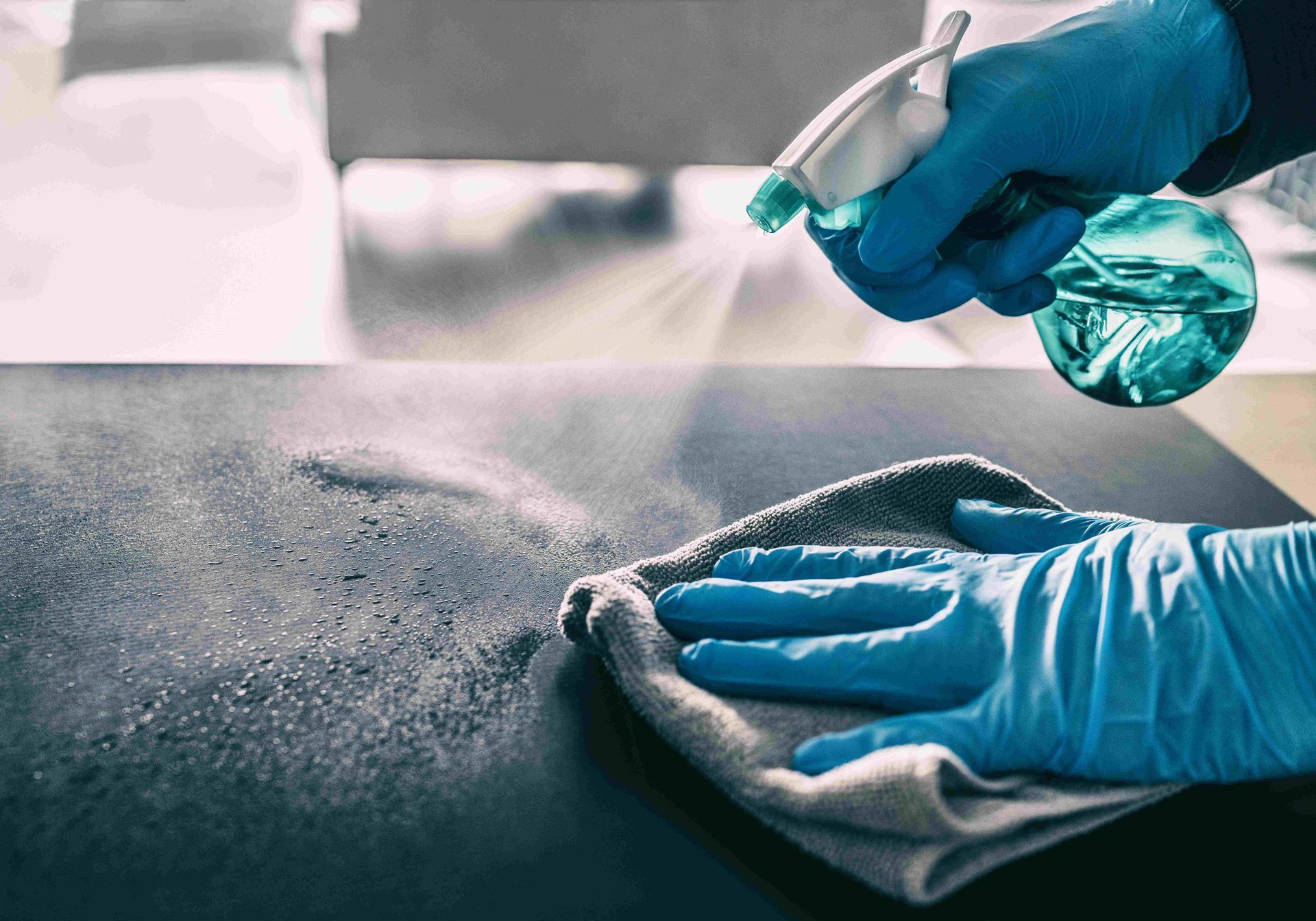 a person wearing blue gloves is cleaning a table with a cloth and spray bottle