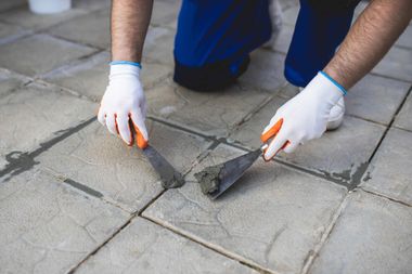 a man is kneeling down and using a spatula to spread cement on a tiled floor