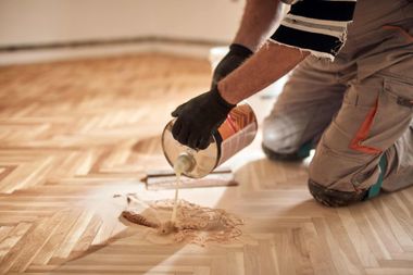 a man is pouring paint on a wooden floor