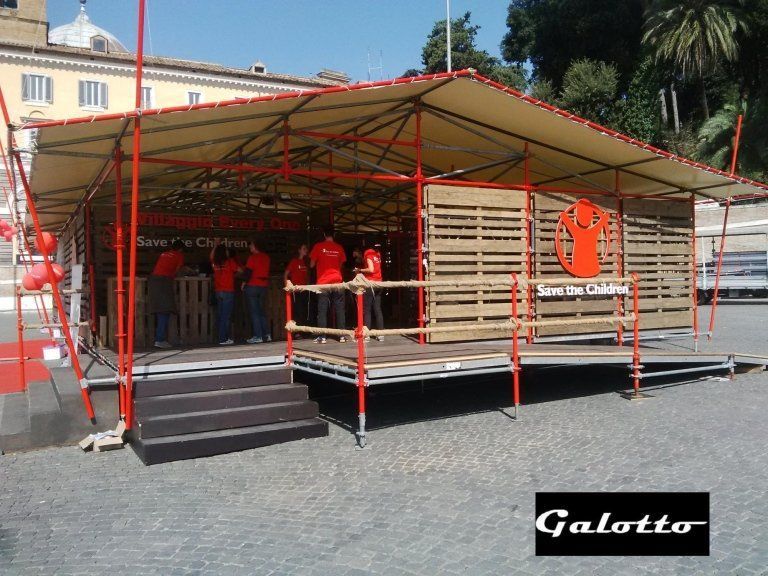 Stage with wooden pallet walls, red scaffolding. People in red shirts inside. 
