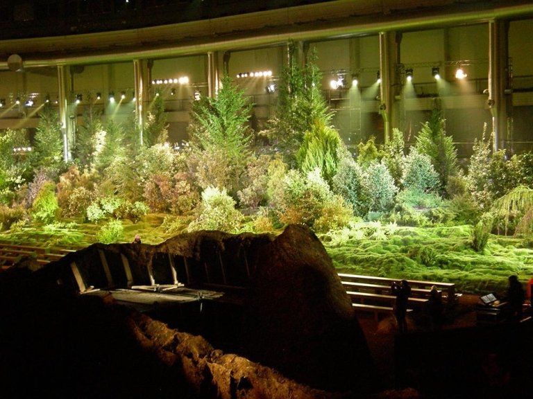 Stage set: Lush forest backdrop with varied trees, grasses, and lighting, viewed from a dark foreground.