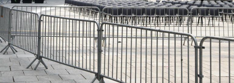 Metal barriers lined up on a paved surface, separating an area with rows of chairs.