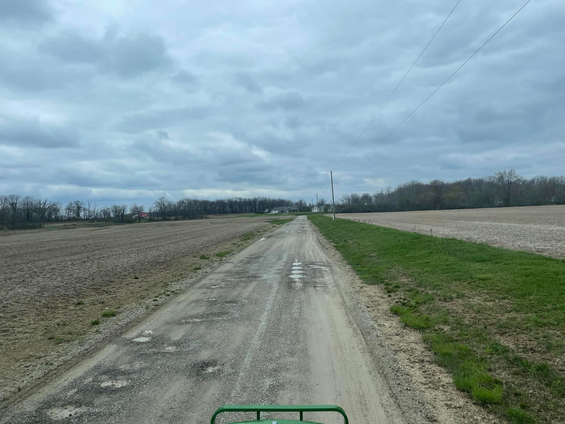 Gravel road through agricultural fields under an overcast sky.