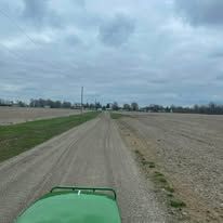 Green tractor on a dirt road between fields under a cloudy sky.