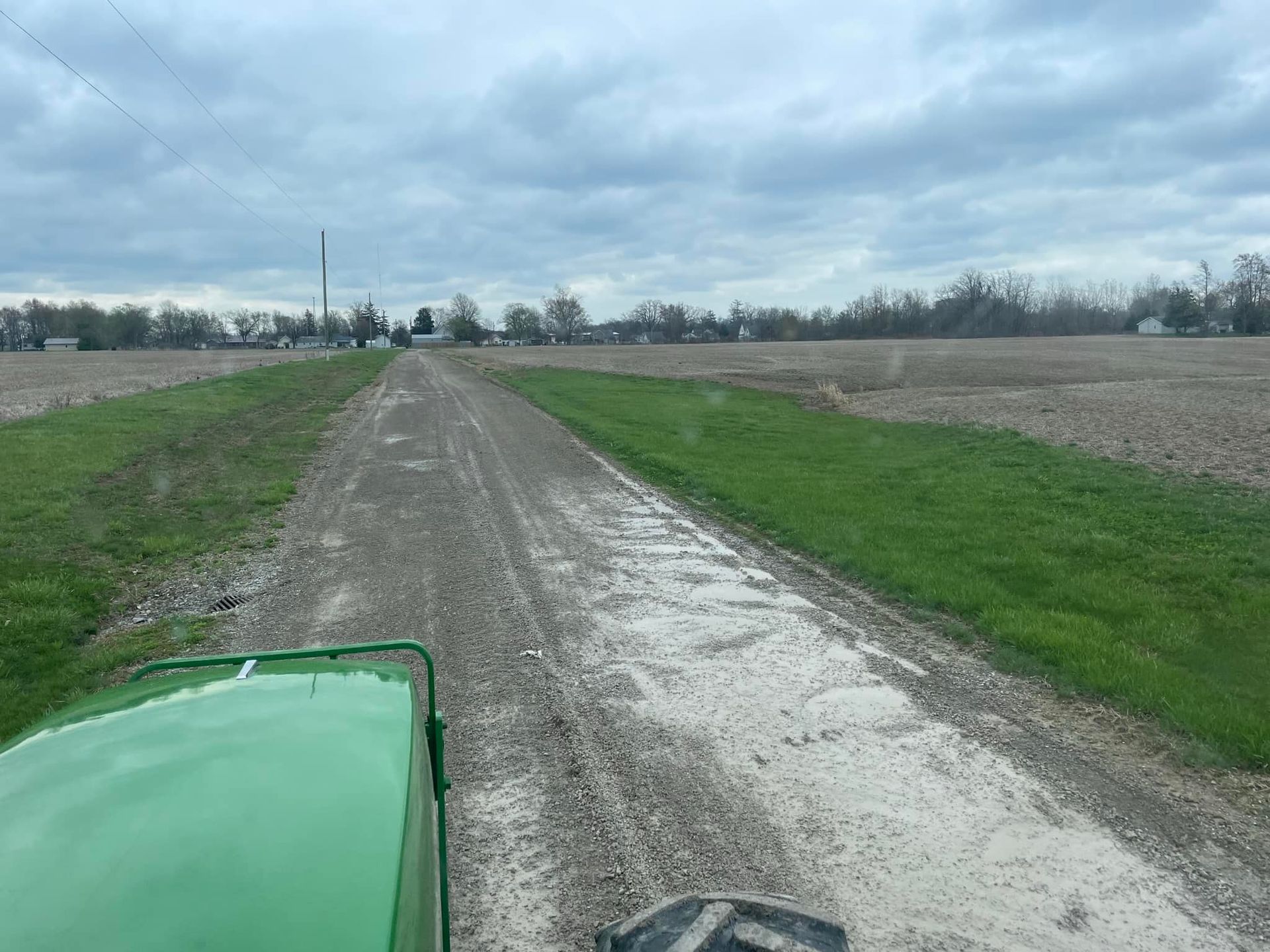 Gravel road between fields from a green tractor, cloudy sky overhead.