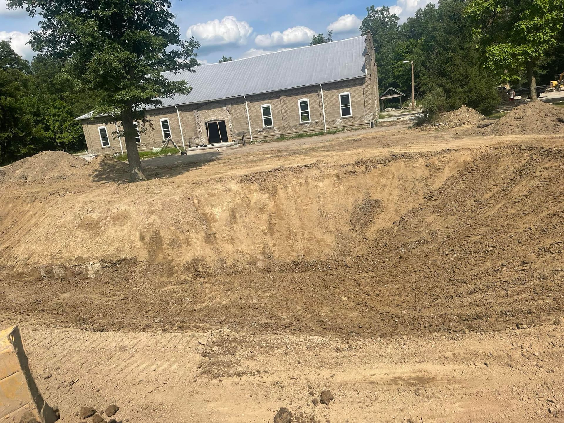 Excavated earth in foreground, building with gray roof in background on a sunny day.