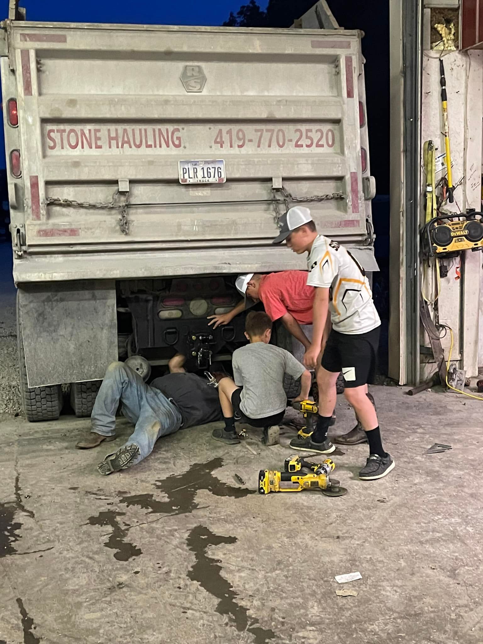 Men working on the undercarriage of a Stone Hauling truck at night.