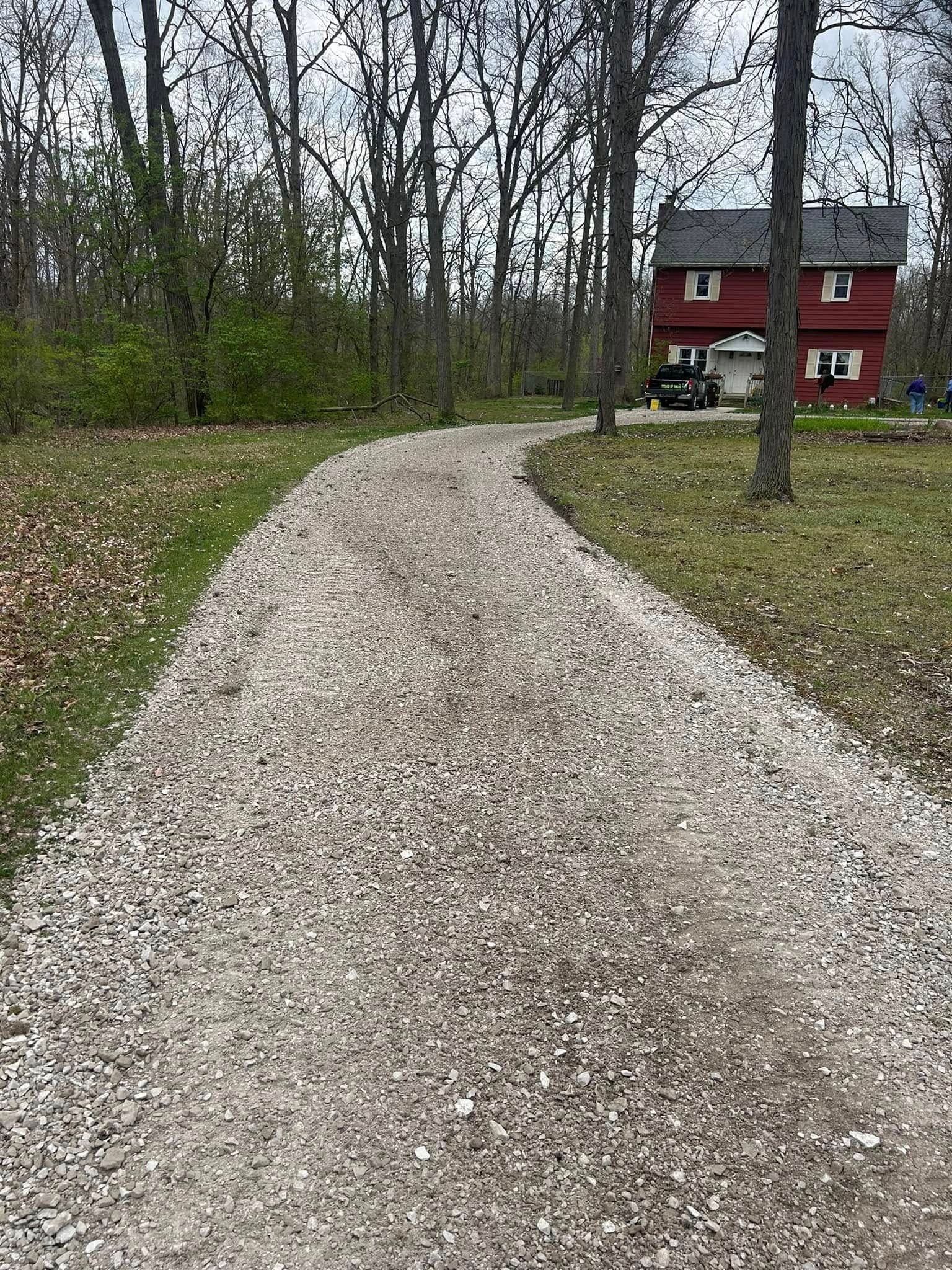 A gravel driveway leads to a red two-story house nestled among trees.