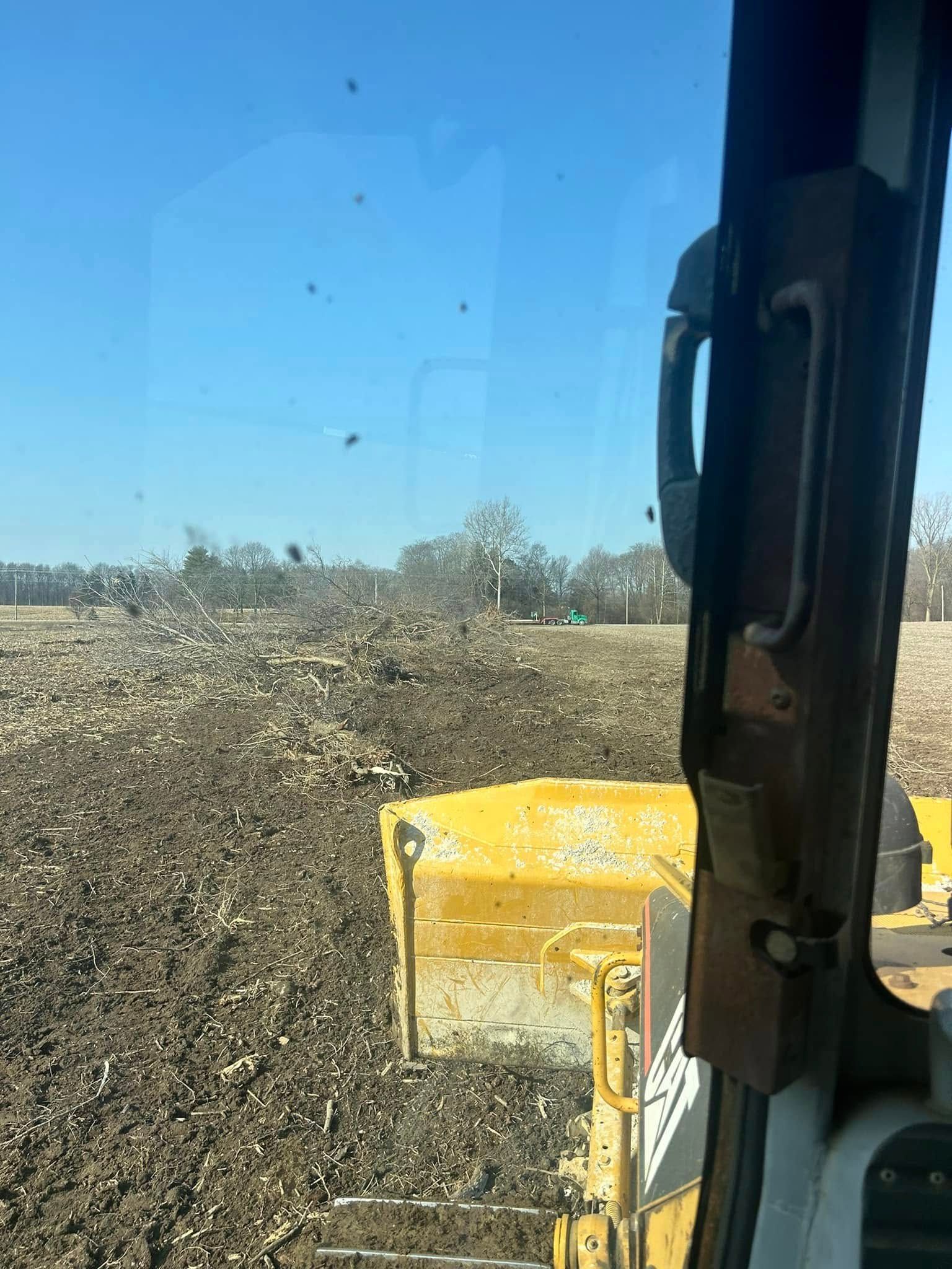View from a tractor cab as it pushes a pile of dirt across a field under a blue sky.