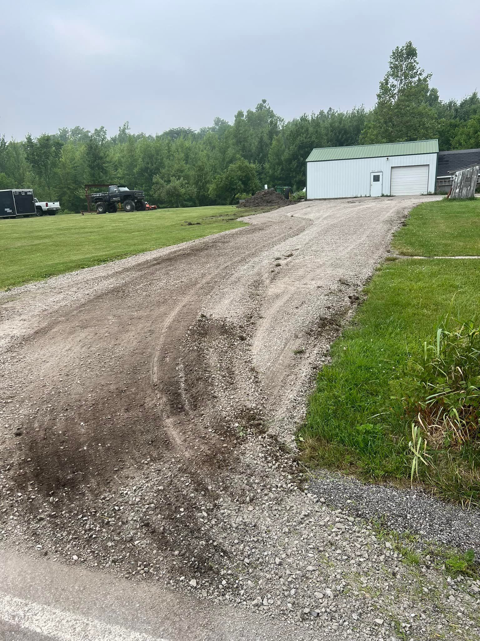 Gravel driveway leading to a white building with green roof, trees in the background, overcast sky.