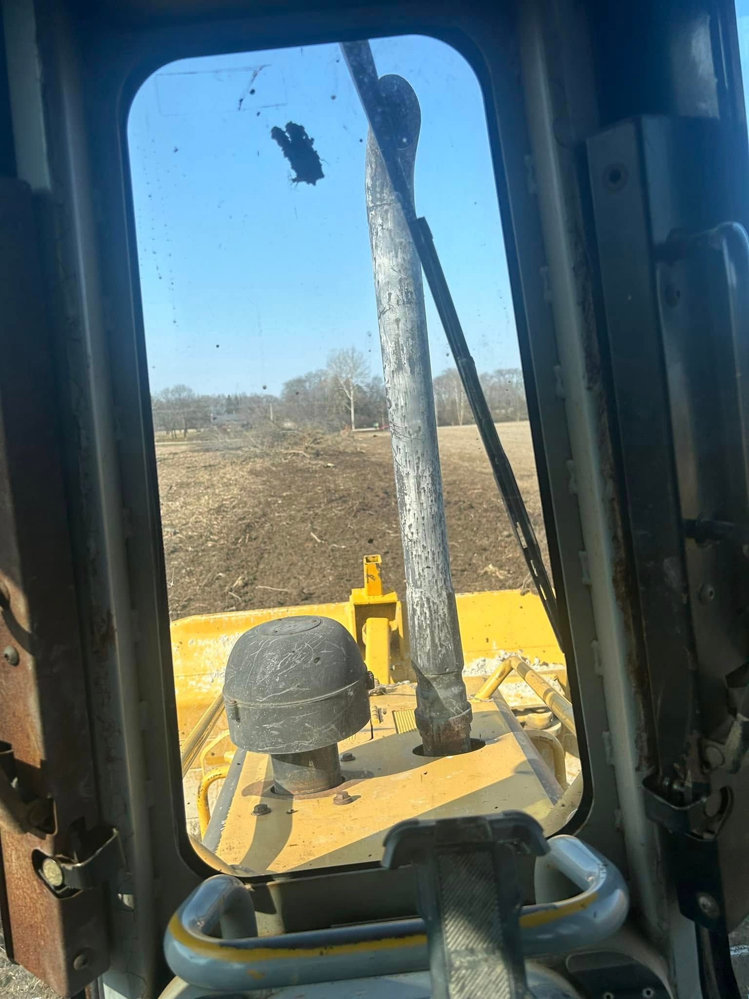 View from inside a yellow bulldozer cab, looking out at a field.