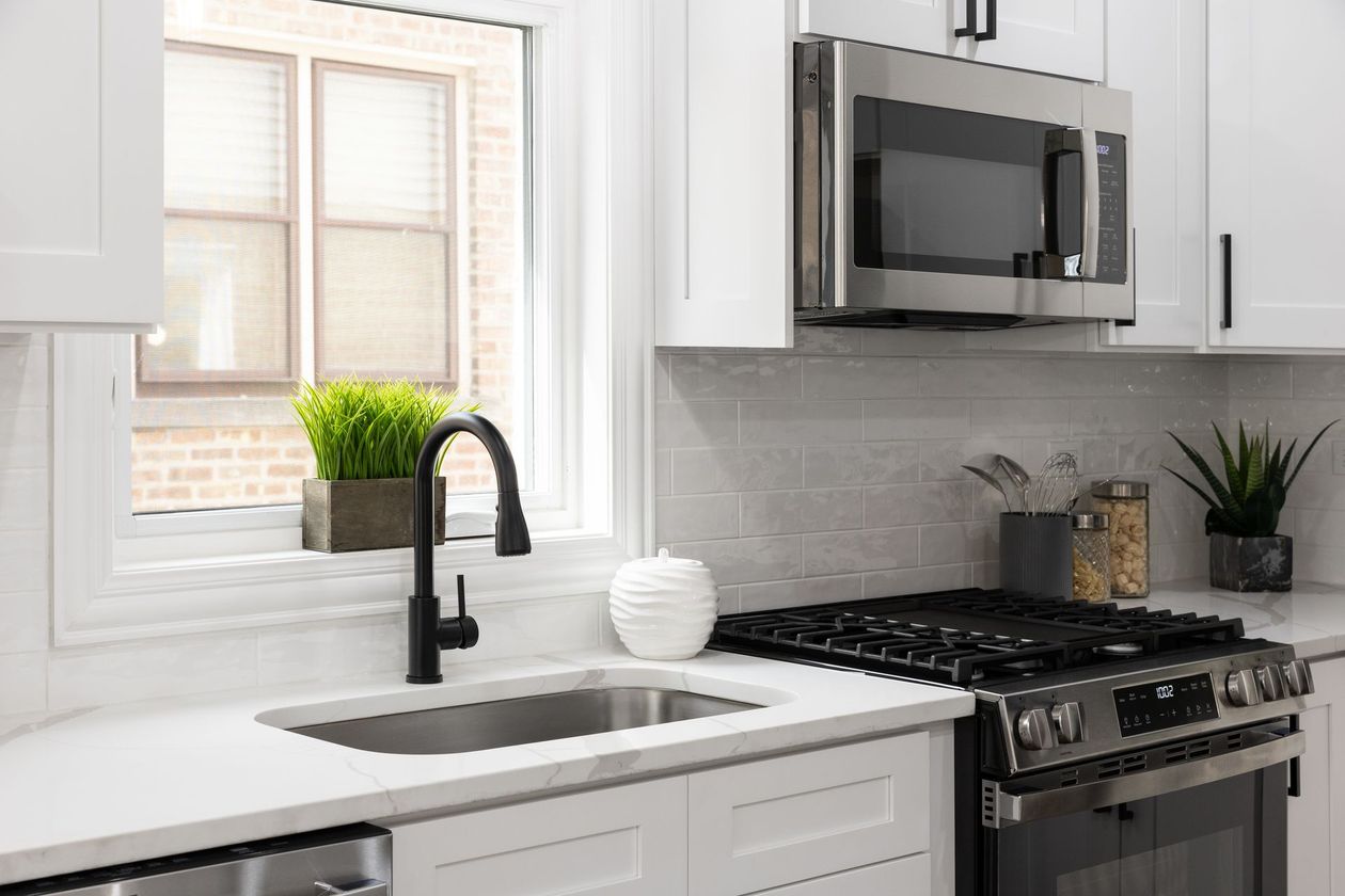A kitchen with a sink , stove , microwave and window.
