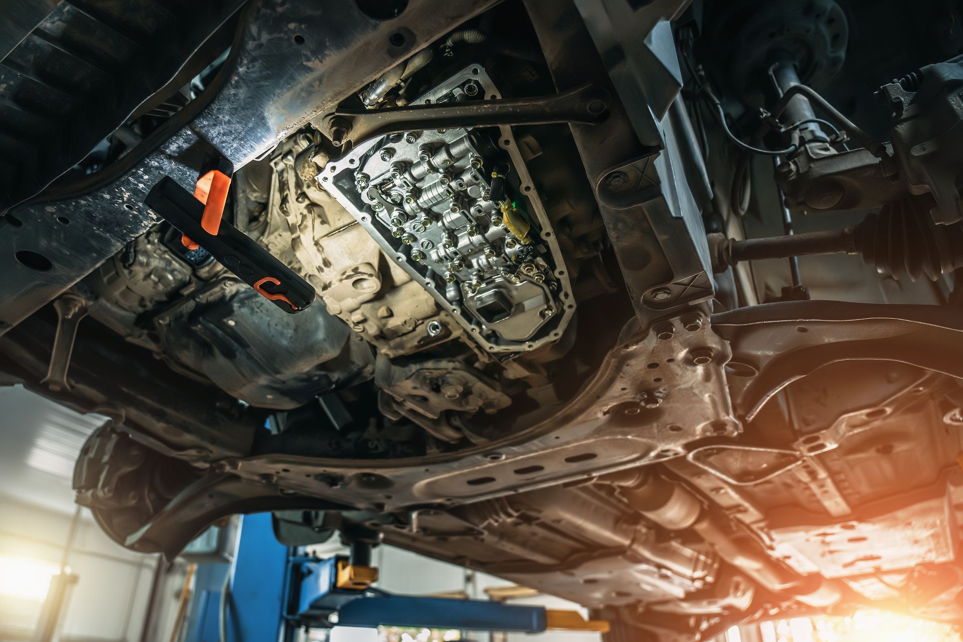 Underside of a vehicle being inspected, illuminated by a work light, in a repair shop.