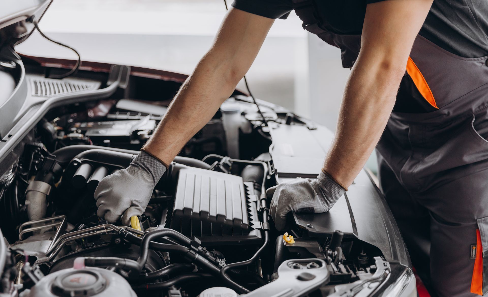 Mechanic inspecting a car engine with gloves on in a repair shop.