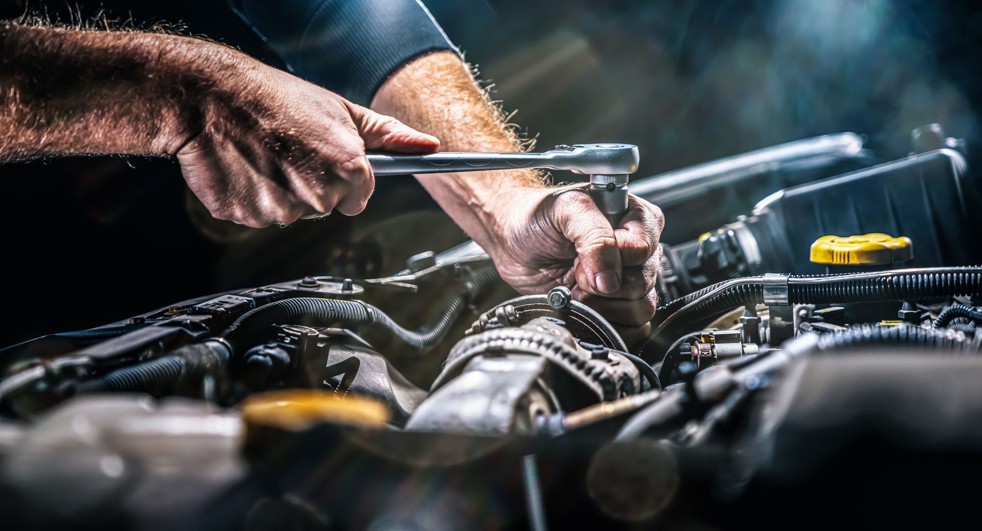 Mechanic using a wrench on a car engine, focused action shot with warm lighting.