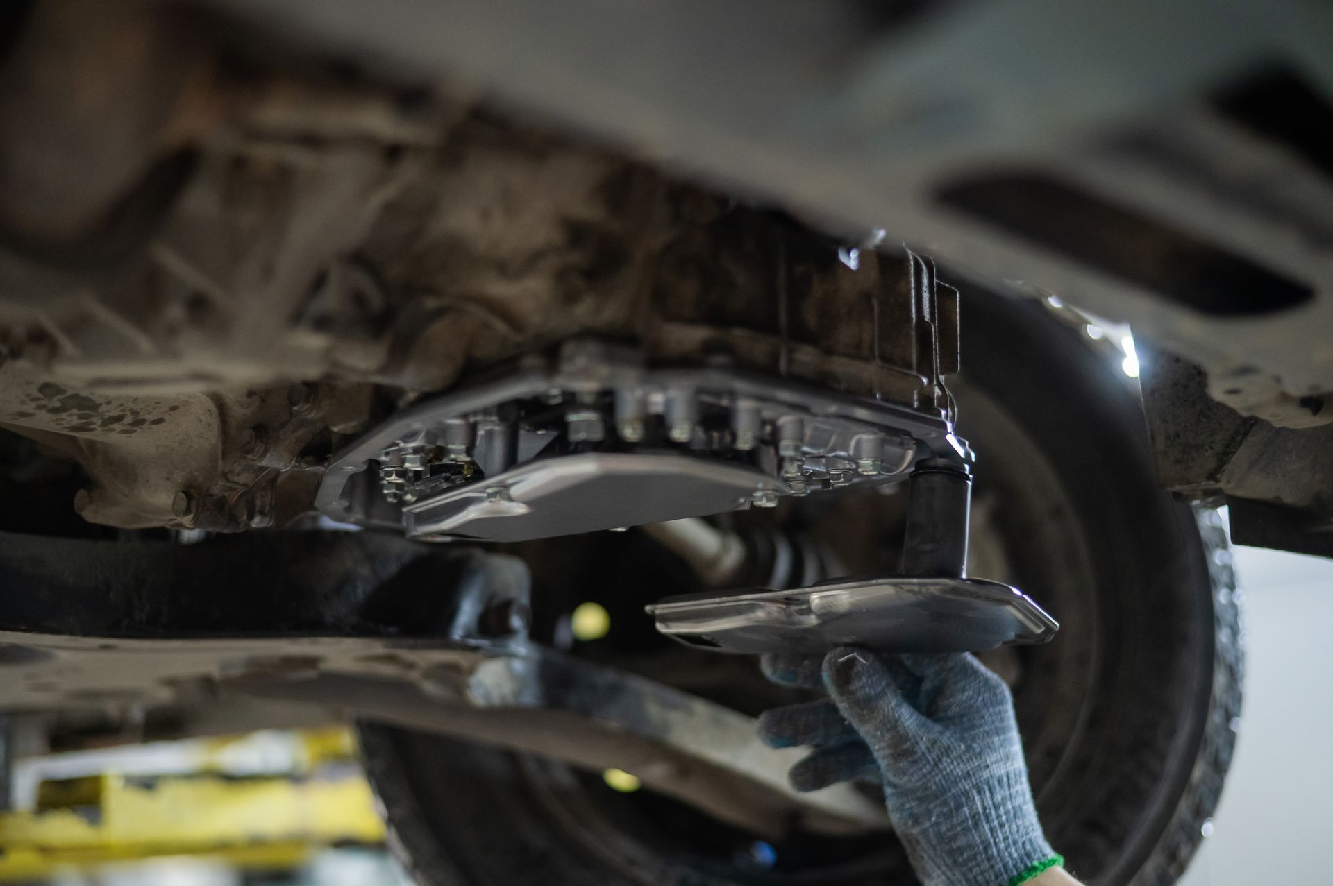 Mechanic removing a transmission pan from a car, visible from underneath.
