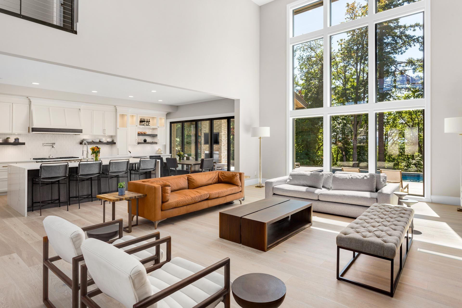 Bright modern living room with tall windows, tan sofa, fireplace, and open kitchen area