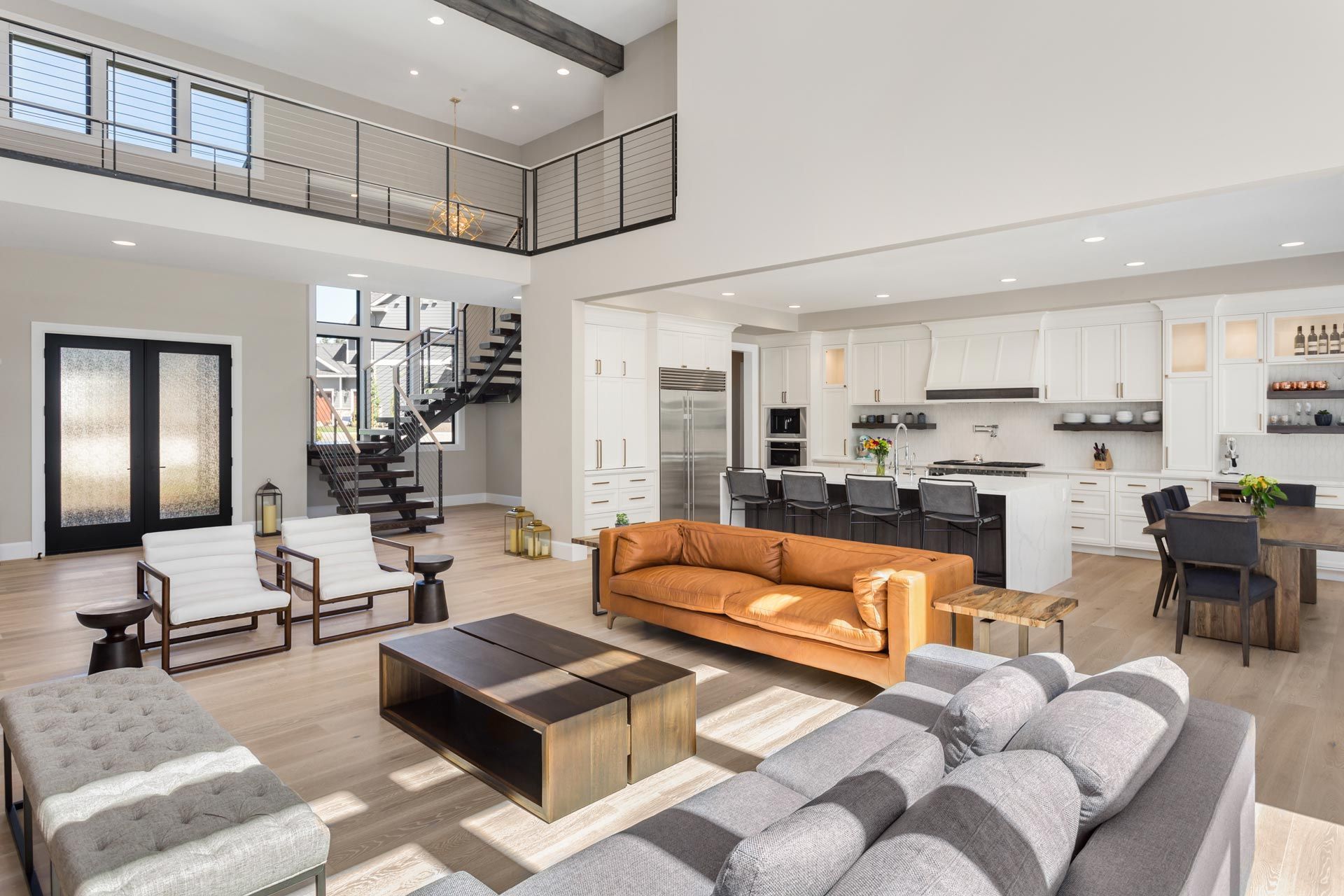 Modern open-plan living room with gray sectional, tan sofa, staircase, and kitchen island