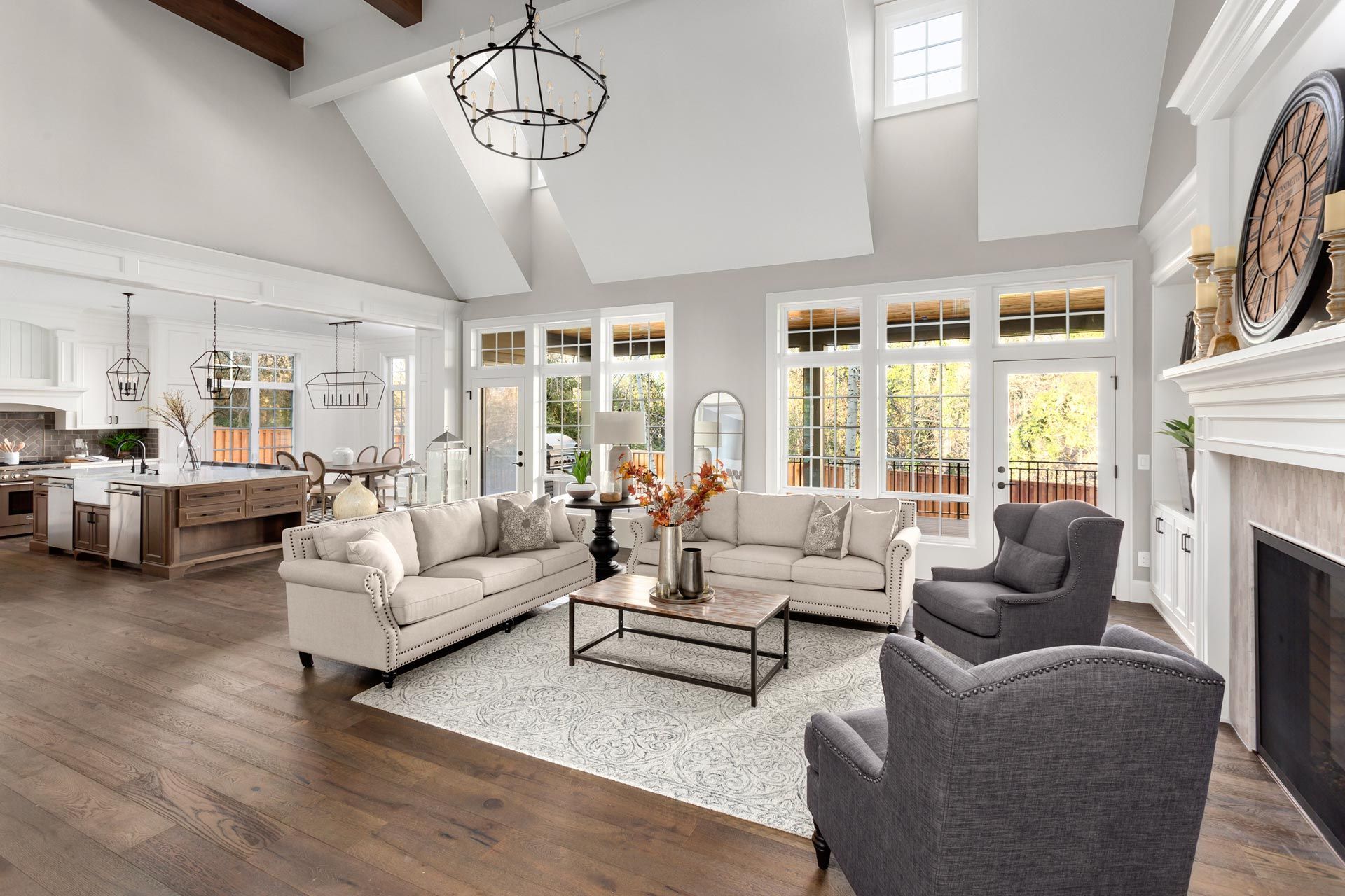 Bright modern living room with white sofas, gray chairs, high ceilings, and large windows overlooking a garden