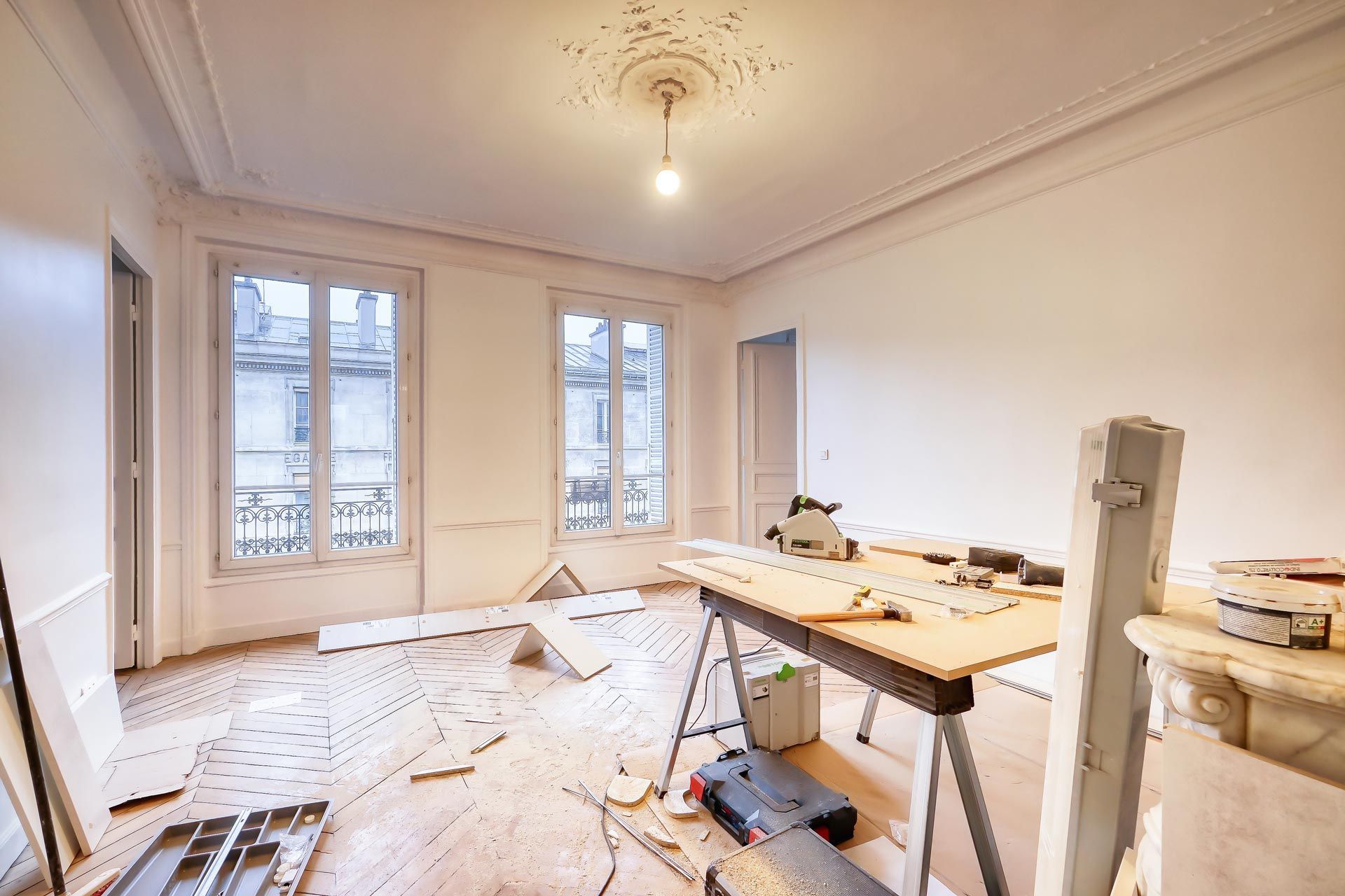 Renovated room with tools, ladders, and unfinished flooring near tall windows