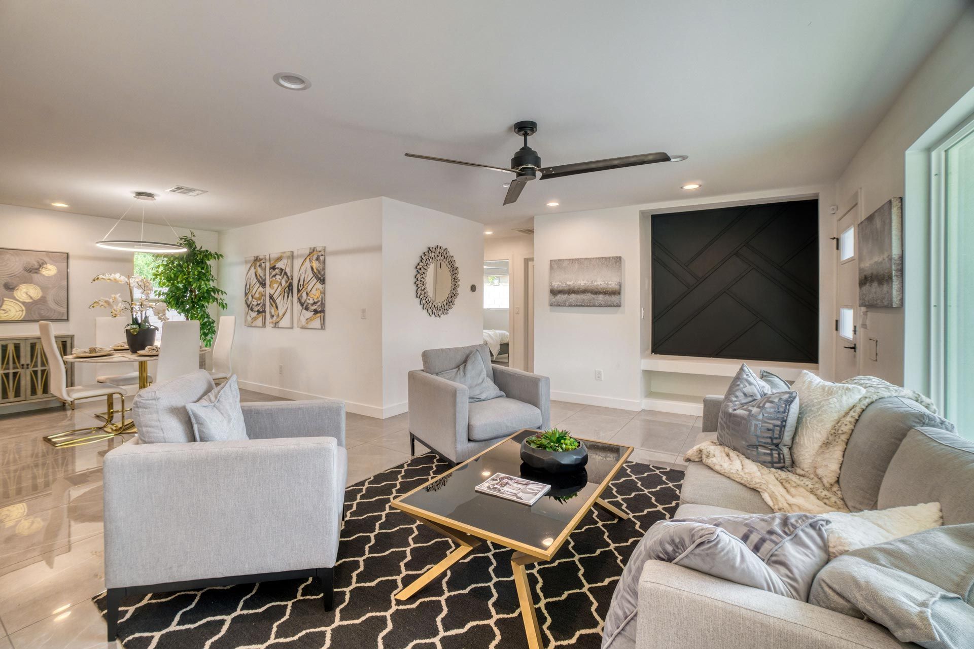 Bright modern living room with gray chairs, beige sofa, black patterned rug, and large wall art.