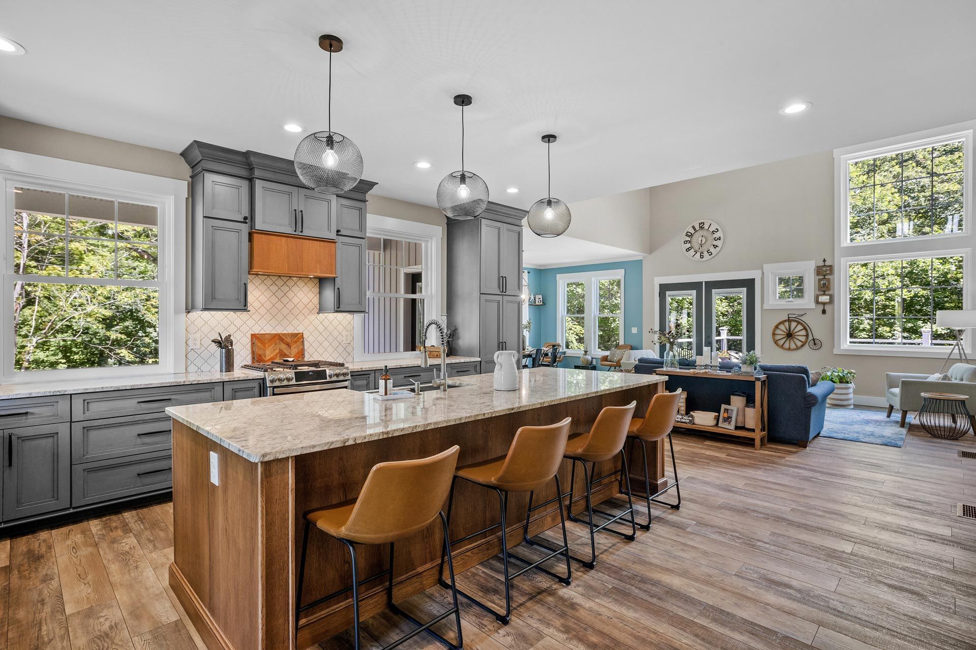 Modern kitchen and living area with large island, pendant lights, blue sofa, and tall windows
