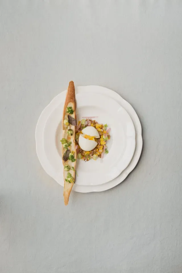 Un plato blanco rematado con un sándwich y un huevo sobre una mesa.