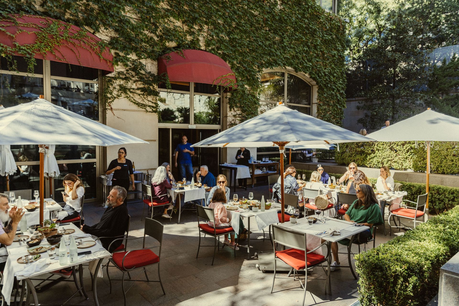 Un grupo de personas están sentadas en mesas bajo sombrillas afuera de un restaurante.