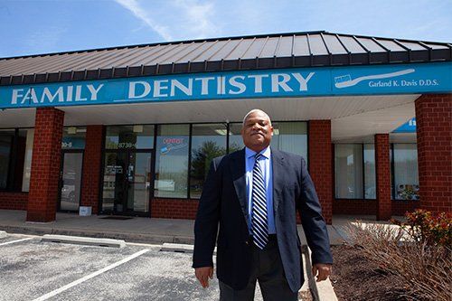 Dr. Davis in a suit and tie is standing in front of a family dentistry building.