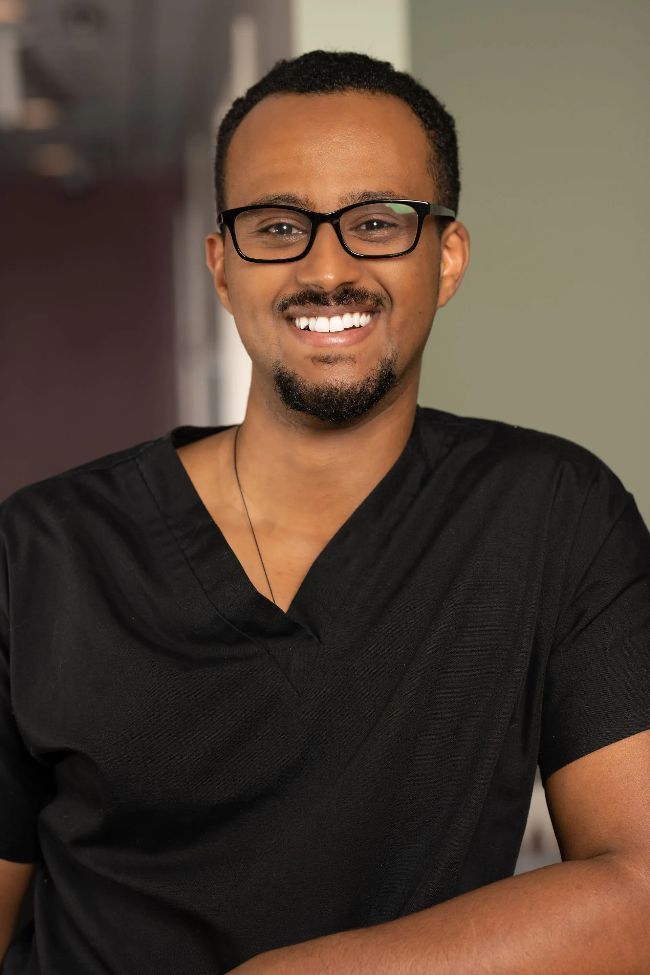 Dr. Kiru wearing glasses and a black shirt is smiling for the camera.