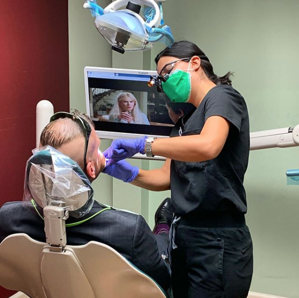 A woman wearing a green mask is working on a man 's teeth