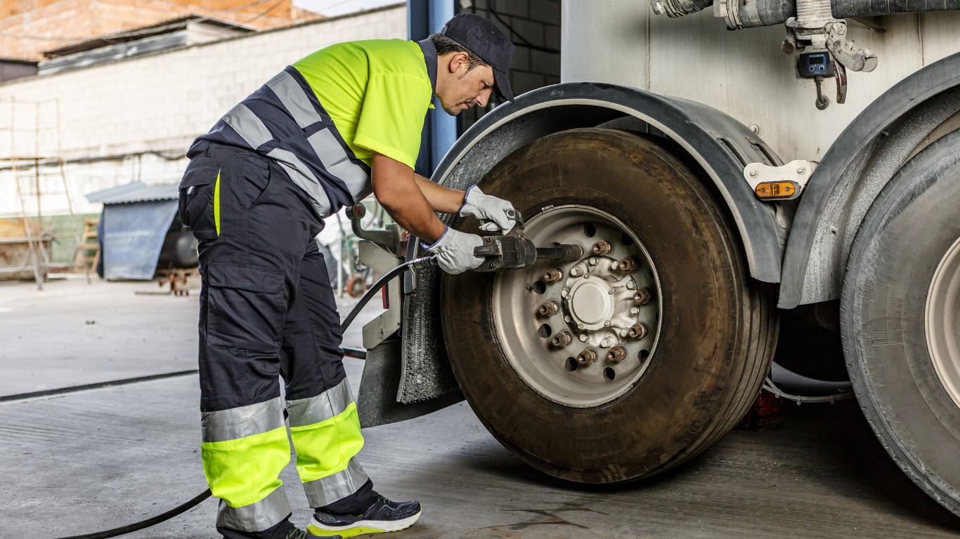 Mechanic in safety vest inflates a truck tire with an air hose outdoors.