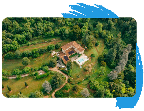 An aerial view of a house in the middle of a forest surrounded by trees. An aerial view of a house in the middle of a forest surrounded by trees.