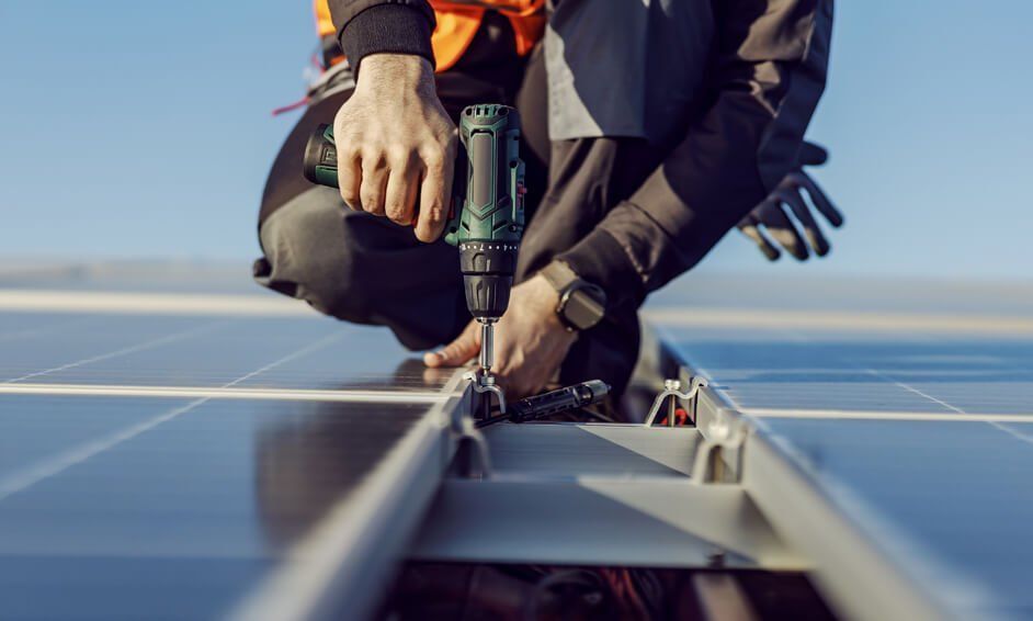 A man is working on a solar panel with a drill.
