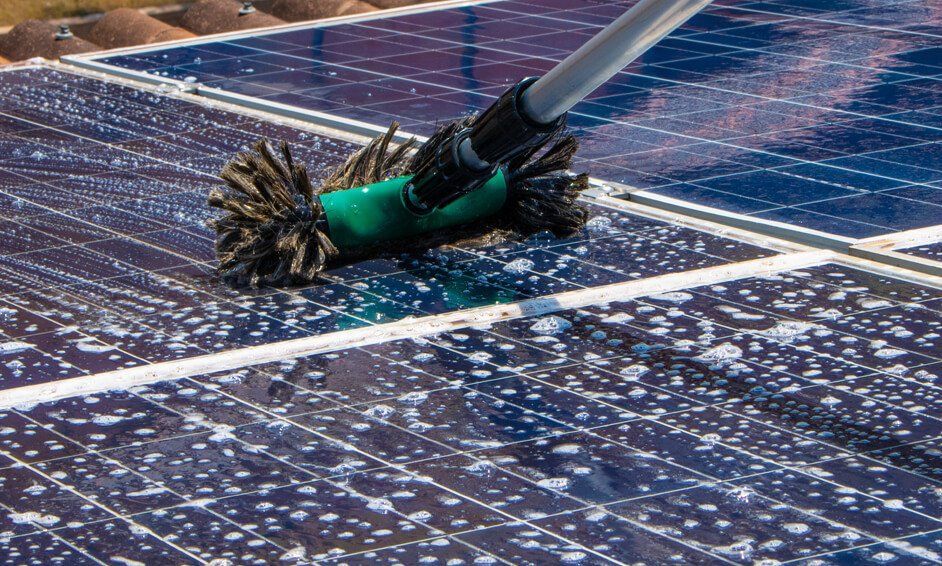 A person is cleaning a solar panel with a brush.