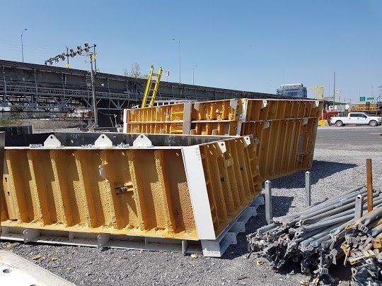 Chantier de construction avec des coffrages jaunes pour le béton, des échafaudages métalliques et un pont.
