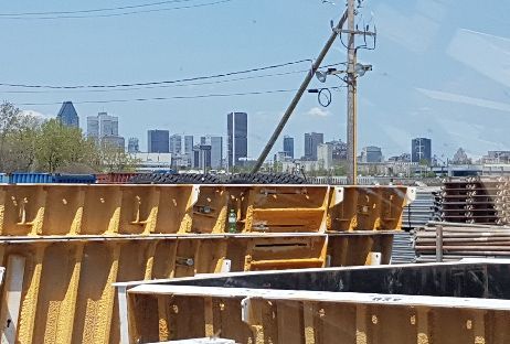 Chantier de construction avec des formes brunes, horizon de la ville en arrière-plan, journée ensoleillée.