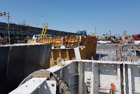 Chantier de construction avec des coffrages en béton, des échafaudages jaunes et un ciel bleu vif.