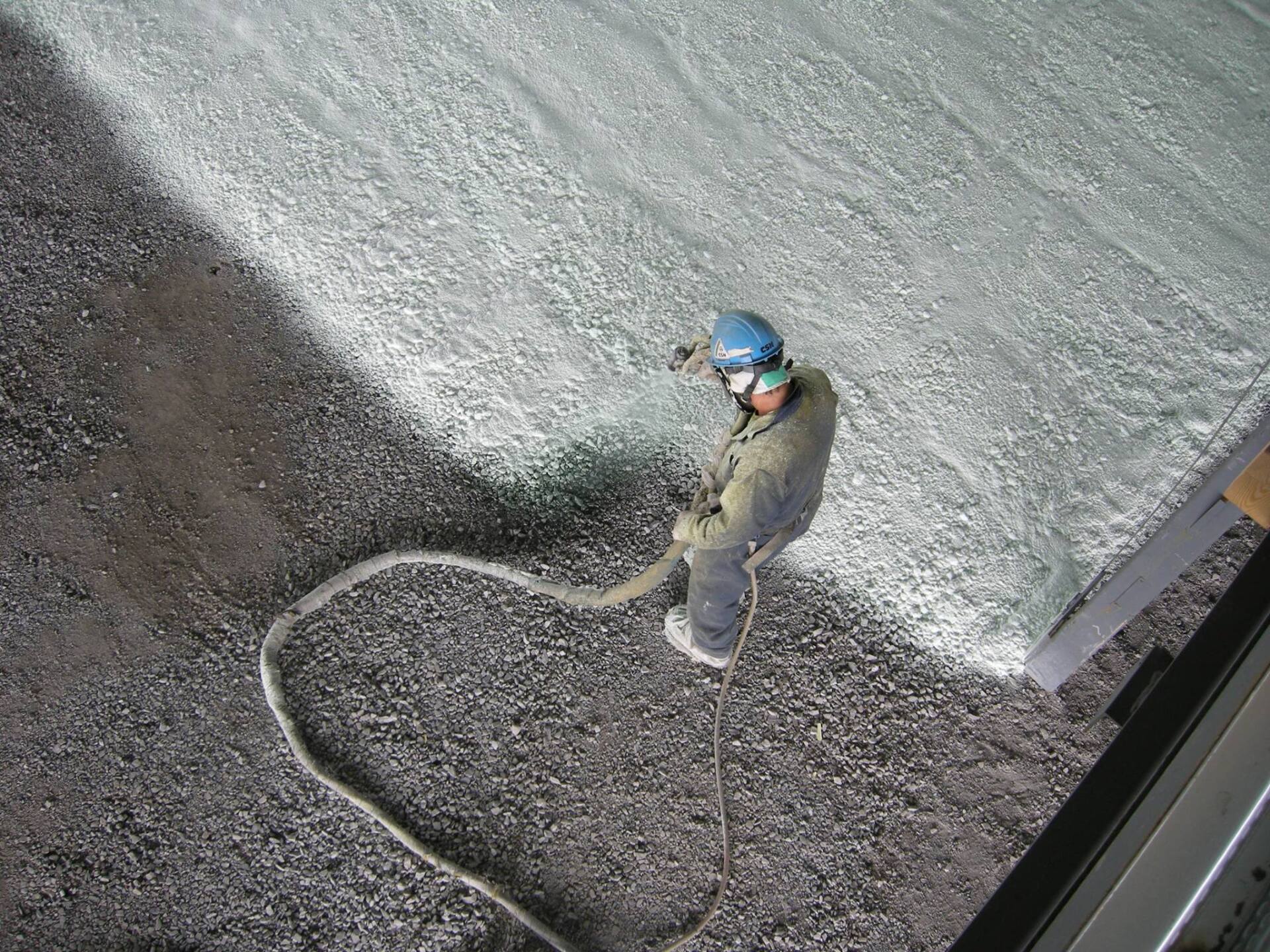 Un ouvrier pulvérise de la mousse isolante sur un toit, portant un équipement de sécurité et attaché à une corde.