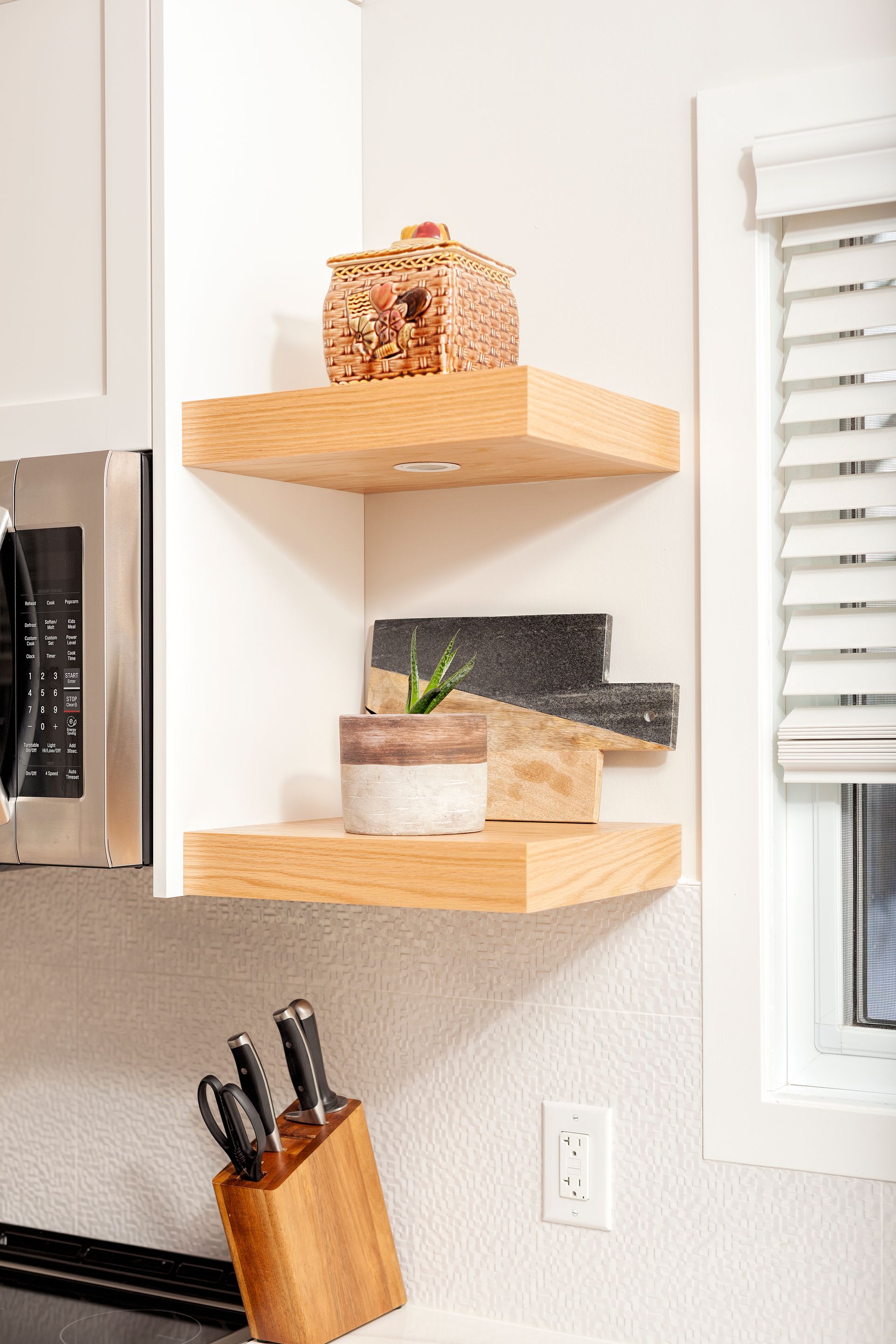 Corner shelves with decor: basket, potted plant, and abstract art pieces. Oak shelves against white wall.