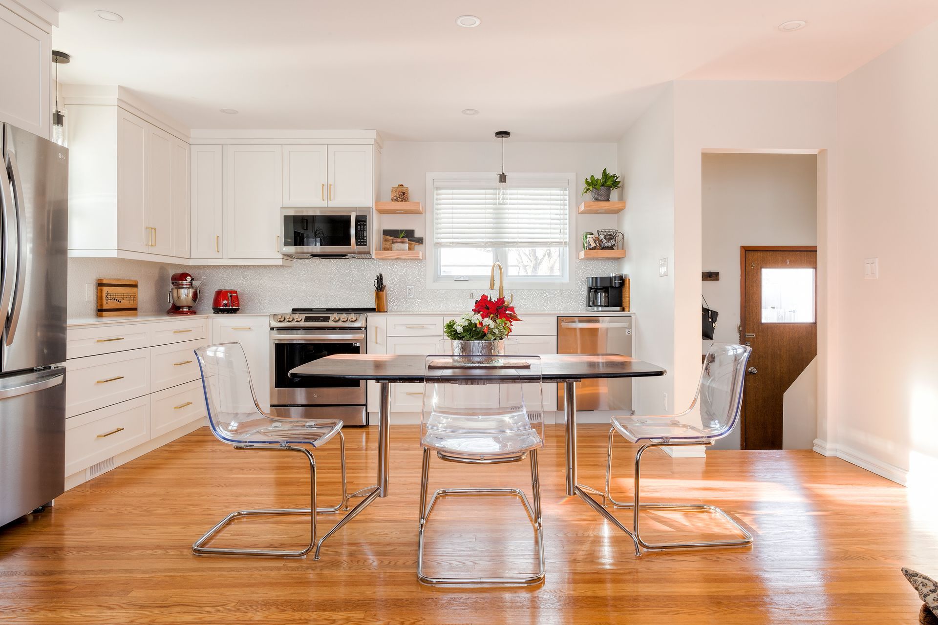 Modern kitchen with white cabinets, stainless steel appliances, wood floor, and acrylic chairs at a table.