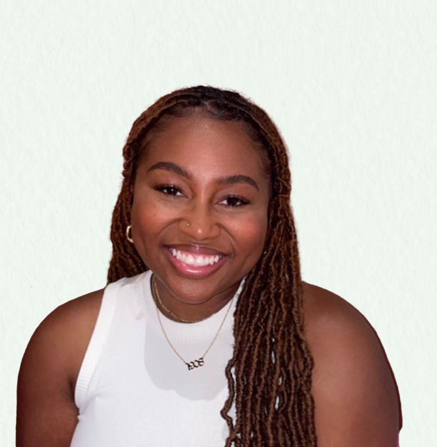 Woman with long brown locs, smiling, wearing a white tank top and gold jewelry.