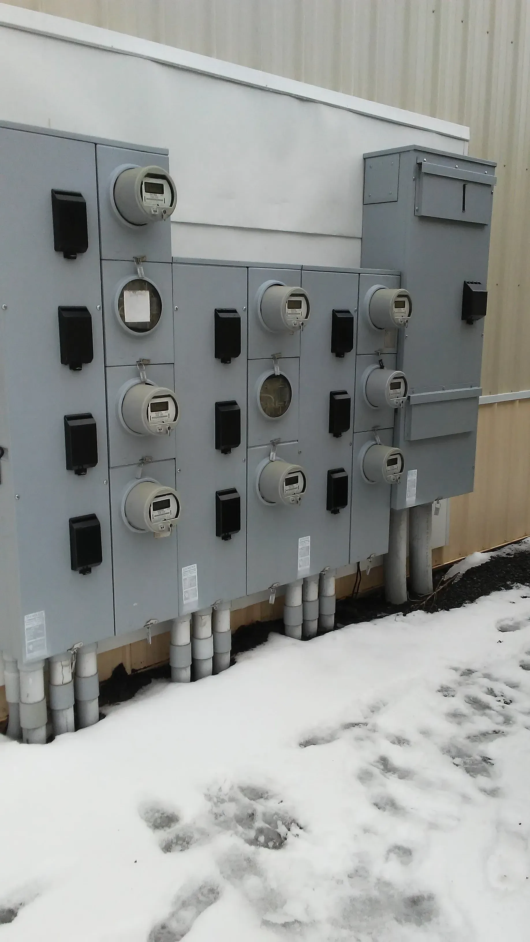 A row of electrical boxes on the side of a building covered in snow.