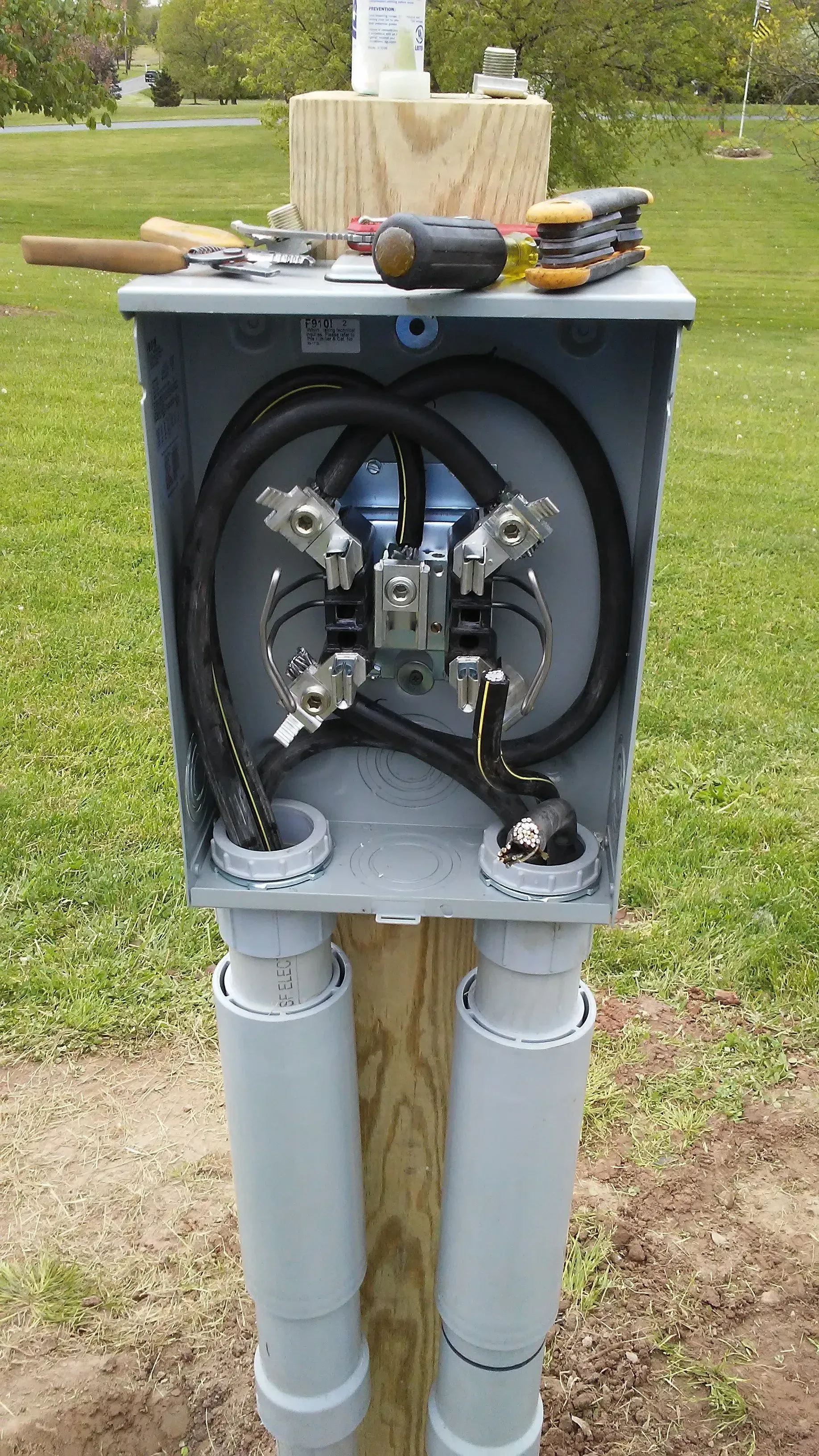 A meter box is sitting on top of a wooden post in the grass.
