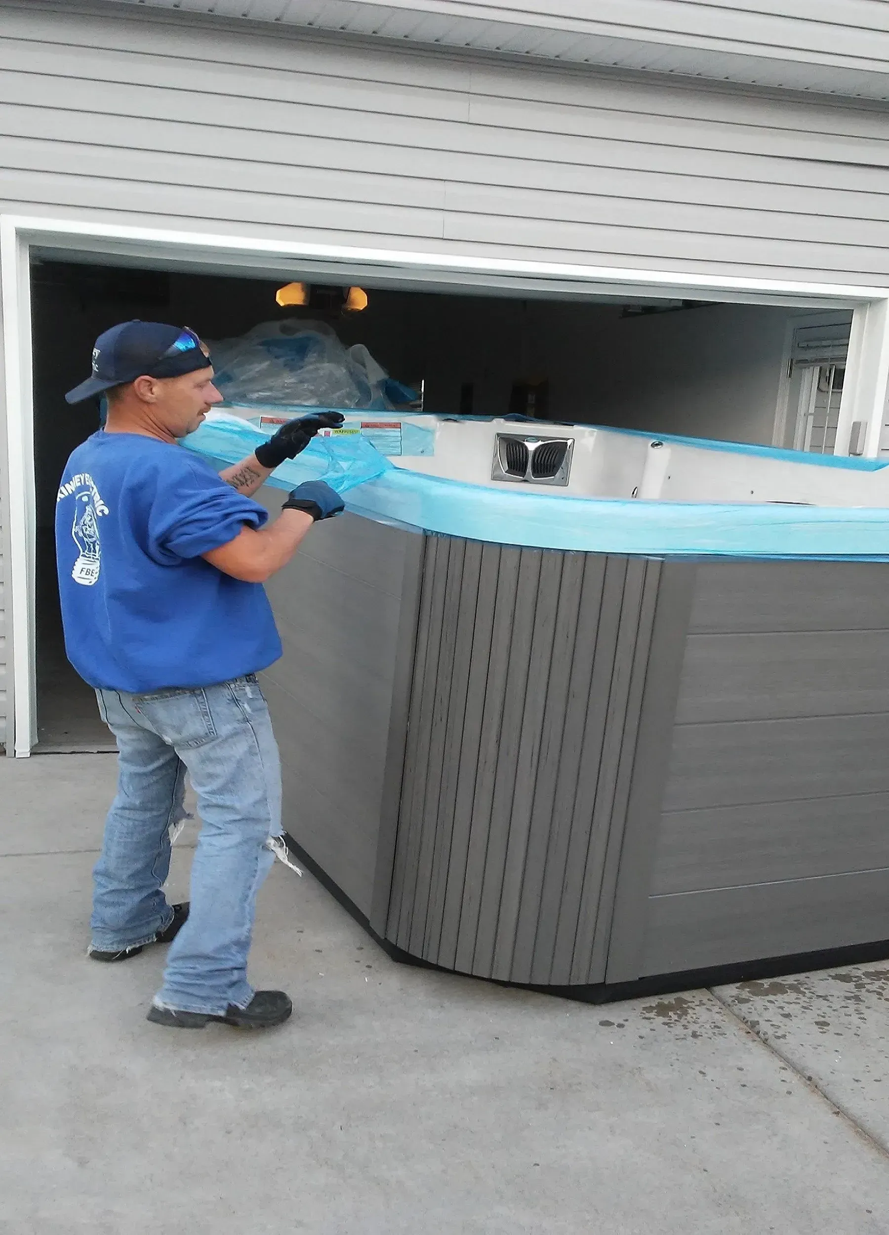 A man in a blue shirt is carrying a hot tub out of a garage