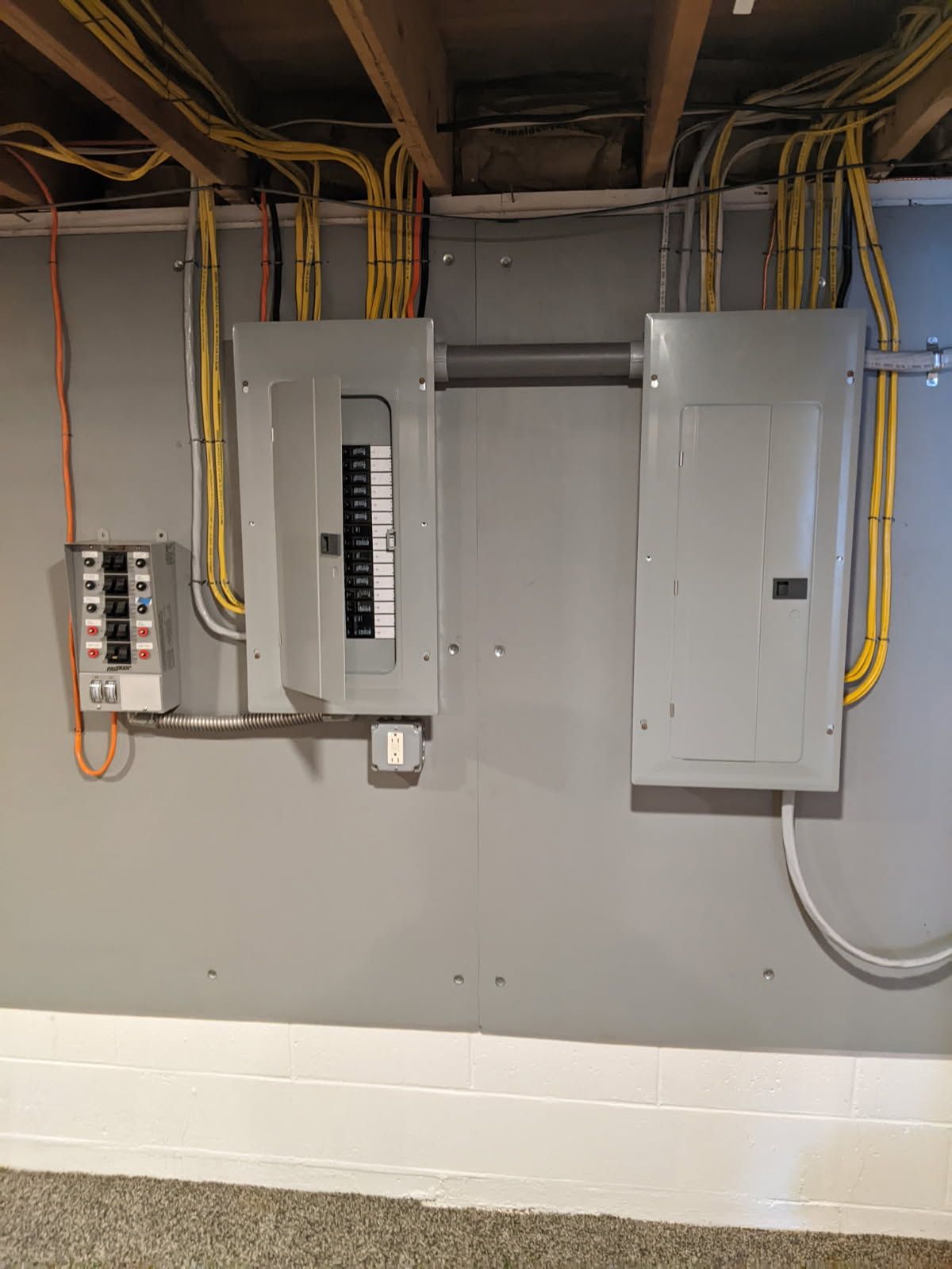 A basement with electrical panels and wires hanging from the ceiling.