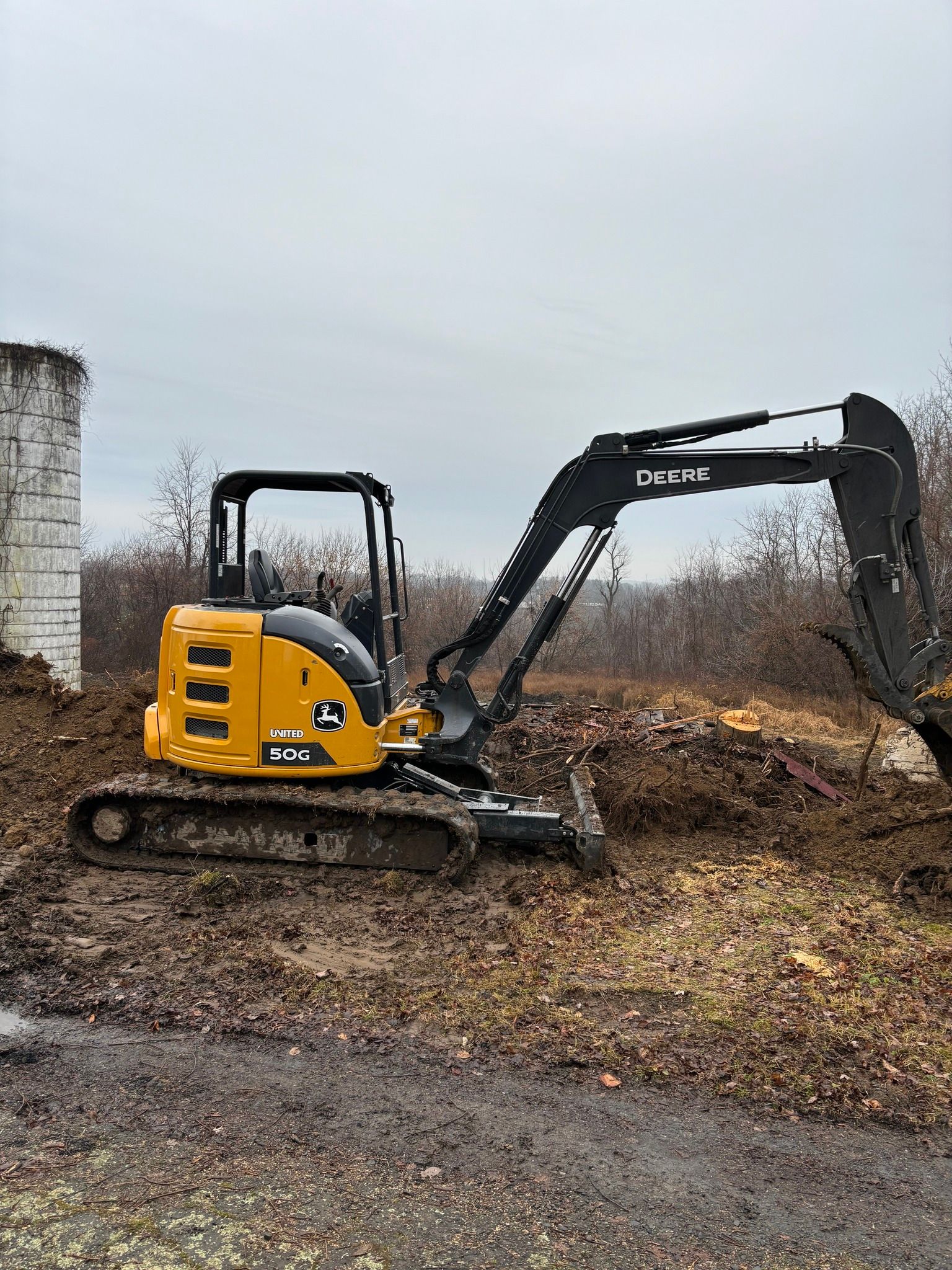 Yellow and black John Deere excavator working on muddy ground.