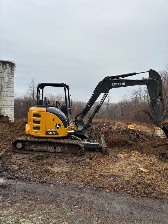 Yellow and black John Deere excavator working on muddy ground.