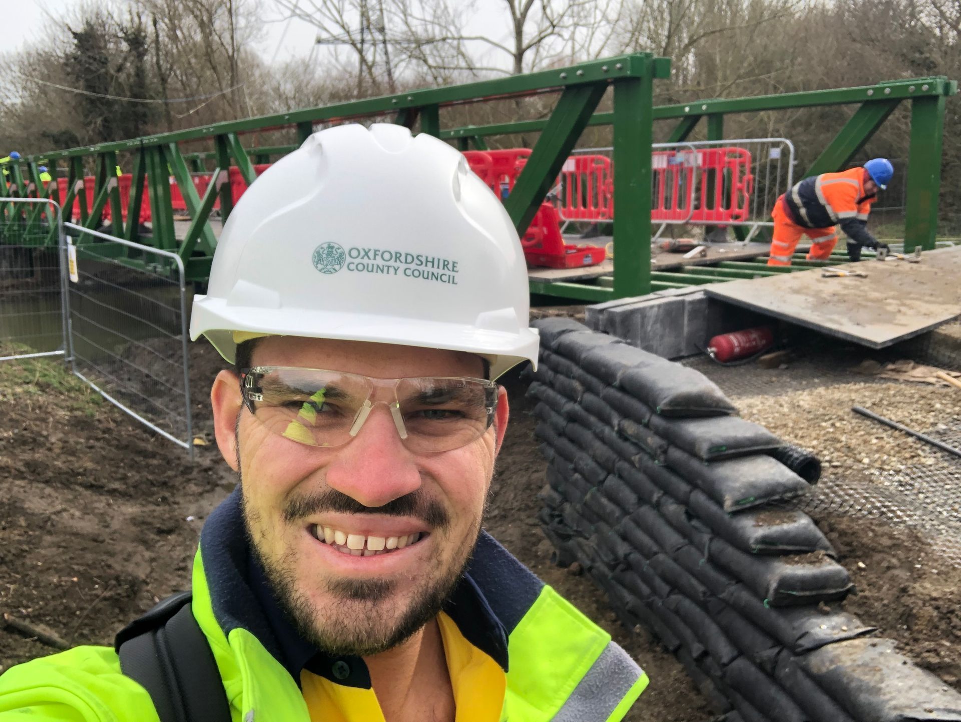 Tradesman pictured in front of bridge construction smiling.