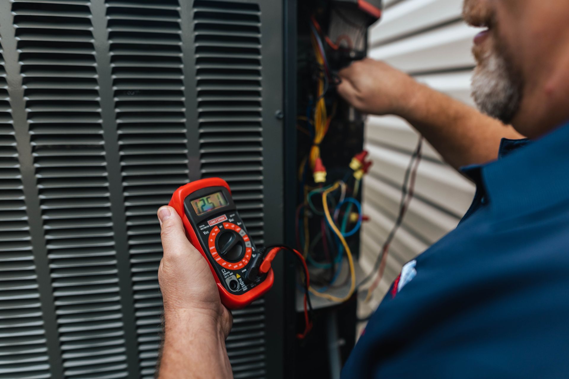 A man is holding a multimeter in front of an air conditioner.